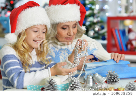 Grandmother and granddaughter in Santa hats making New Year's decorations Grandmother and granddaughter in Santa hats making New Year's decorations 109638859