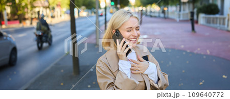 Close up portrait of beautiful young woman, blonge girl walking on street with mobile phone, chatting with friend, has happy face expression while talking over cellphone on her way Close up portrait of beautiful young woman, blonge girl walking on street with mobile phone, chatting with friend, has happy face expression while talking over cellphone on her way 109640772