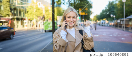 Close up portrait of beautiful young woman, blonge girl walking on street with mobile phone, chatting with friend, has happy face expression while talking over cellphone on her way 109640891
