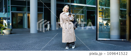 Lifestyle portrait of young beautiful woman, waiting for someone on street, holding smartphone, using mobile phone, ordering taxi in application 109641522