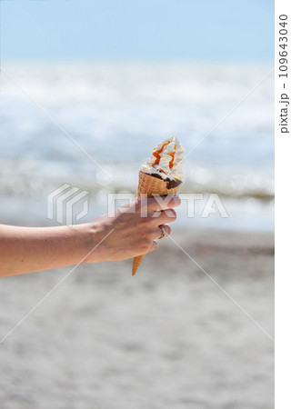 Female hand with ice cream on the background of the beach and sea. Female hand with ice cream on the background of the beach and sea. 109643040