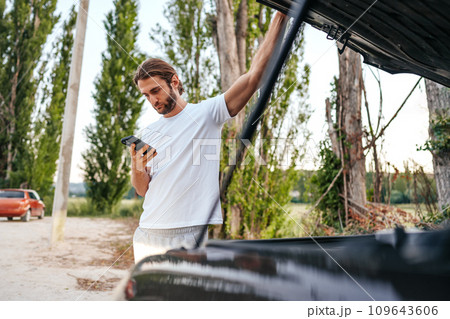 Young man hiker near a broken car on the road with open hood 109643606