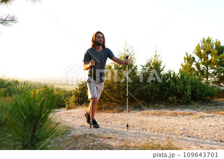 Young man hiker travels through the mountains with trekking poles for nordic walking Young man hiker travels through the mountains with trekking poles for nordic walking 109643701