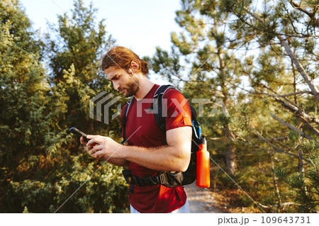 Hiker man with backpack checks the route on his phone on the walking trail 109643731