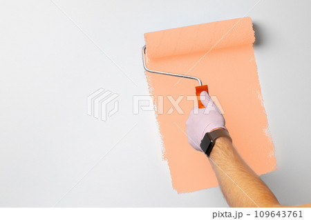 Gloved male hand painting wall into peach fuzz color of the year 2024 Gloved male hand painting wall into peach fuzz color of the year 2024 109643761
