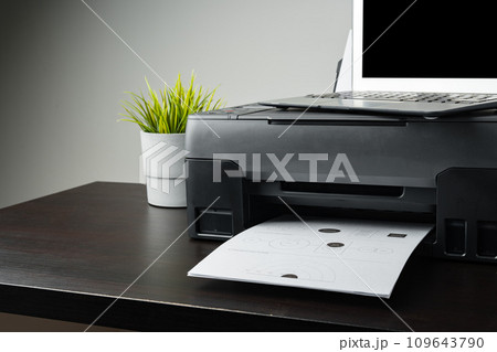Modern printer with paper and laptop on table in office Modern printer with paper and laptop on table in office 109643790