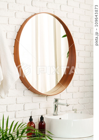 Bathroom interior with circle shaped mirror in wooden frame and white sink Bathroom interior with circle shaped mirror in wooden frame and white sink 109643873