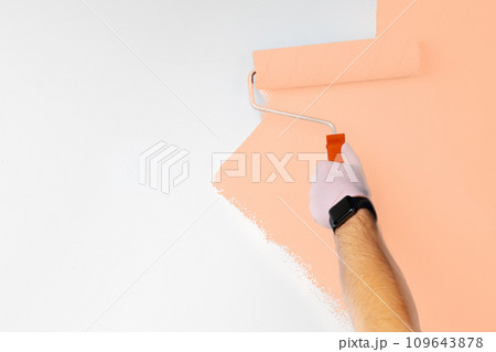 Gloved male hand painting wall into peach fuzz color of the year 2024 Gloved male hand painting wall into peach fuzz color of the year 2024 109643878