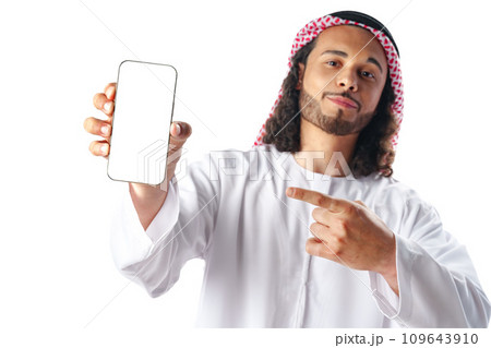 Young Arab man in traditional dress thobe showing smartphone with blank screen isolated on white background Young Arab man in traditional dress thobe showing smartphone with blank screen isolated on white background 109643910