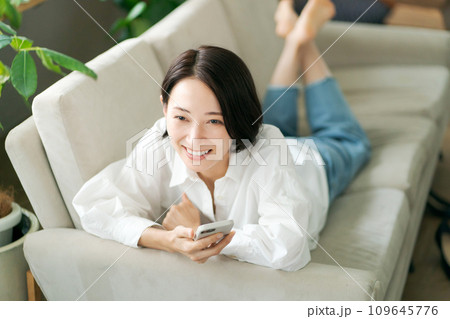 ソファに寝そべってスマホを見る女性 ソファに寝そべってスマホを見る女性 109645776