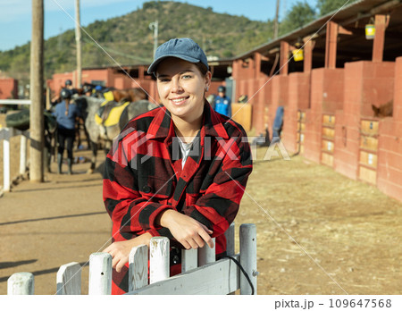 Portrait of female owner of horse farm shows her farm against the backdrop of corral for walking horses 109647568