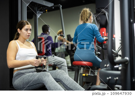 Woman is engaged in a simulator with horizontal weights in gym 109647930