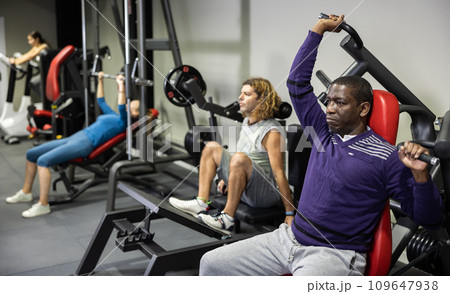 African man doing exercises on shoulder press machine in gym African man doing exercises on shoulder press machine in gym 109647938