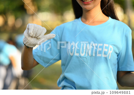 Cropped shot of female pointing to volunteer uniform and smiling over nature background 109649881