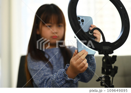 Smiling asian girl talking to camera of mobile phone on tripod, recording lifestyle blog at home 109649895