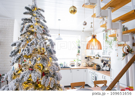 Festive Christmas decor in white kitchen, modern rustic interior with a snowy Christmas tree and fairy lights. New Year, Christmas mood, cozy home. The general plan Festive Christmas decor in white kitchen, modern rustic interior with a snowy Christmas tree and fairy lights. New Year, Christmas mood, cozy home. The general plan 109651656