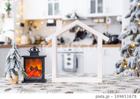 Cozy Christmas decor tiny house of small size on table of festive white modern kitchen. Gift for New Year. Insurance, moving to new house, mortgage, rent and purchase real estate Cozy Christmas decor tiny house of small size on table of festive white modern kitchen. Gift for New Year. Insurance, moving to new house, mortgage, rent and purchase real estate 109651678