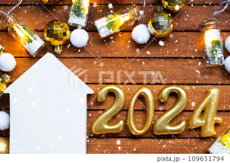 House key with tiny figure of home mock up on festive brown wooden background, lights of garlands. New Year 2024 wooden letters, greeting card. Purchase, construction, relocation, mortgage, insurance 109651794
