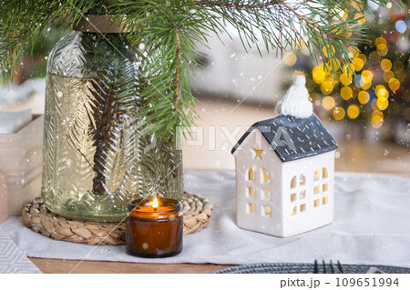 The figure of a tiny cozy house on the table against the background of the Christmas tree lights. New Year, mood, cozy home. The figure of a tiny cozy house on the table against the background of the Christmas tree lights. New Year, mood, cozy home. 109651994