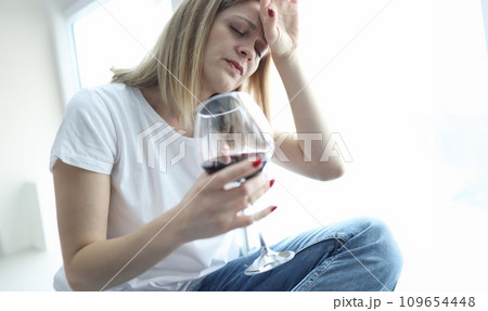 Tired woman with glass of red wine holding her head 109654448