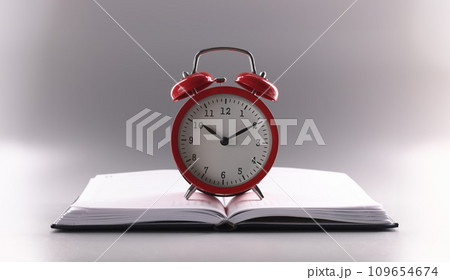Red retro clock stand on top of open notebook or book Red retro clock stand on top of open notebook or book 109654674