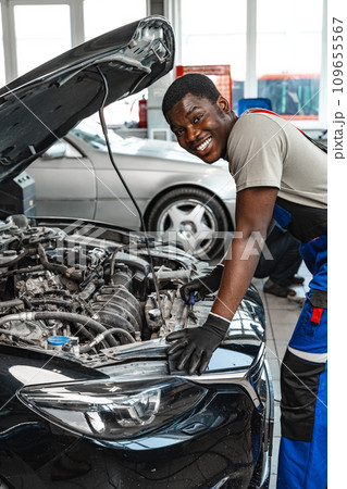 Young African man working under the hood of car fixing engine in auto service 109655567