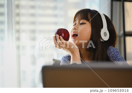Playful asian girl eating apple while studying online on laptop at home. Online education concept. 109658918
