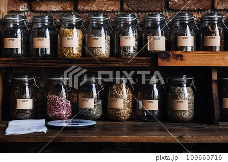 Glass Jars of Assorted Organic Freeze-Dried Foods on Wooden Shelf. Glass jars filled with various dried fruit, Raspberries, herbs and seeds, showcasing an organized pantry setup. 109660716