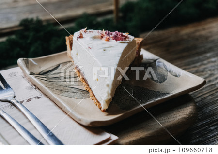 Creamy Cheesecake Slice on Botanical Ceramic Plate. Elegant cheesecake slice topped with dried petals, perfectly presented on a leaf-patterned ceramic plate. 109660718