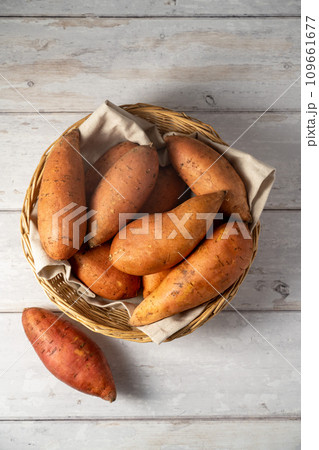 Whole raw sweet potatoes in a basket, on bright background, top view. Whole raw sweet potatoes in a basket, on bright background, top view. 109661677