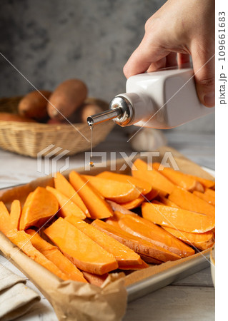 Cooking sweet potato wedges, fries on a baking pan. Hand adding oil. Cooking sweet potato wedges, fries on a baking pan. Hand adding oil. 109661683