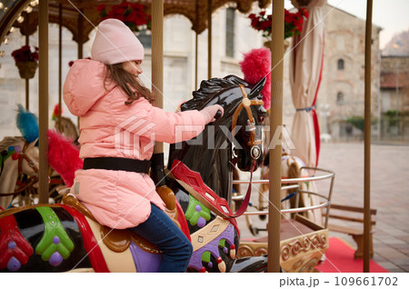 Little child girl riding a wooden horse on a carousel at Christmas funfair. Little child girl riding a wooden horse on a carousel at Christmas funfair. 109661702