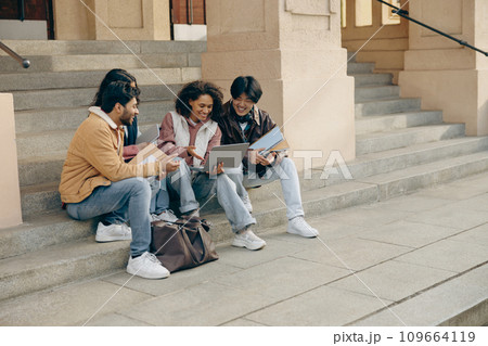 Cheerful students with laptop is studying outdoors sitting near university. Education concept 109664119