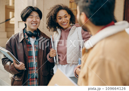 Cheerful students talking and laughing together outdoor standing near campus and holding books  109664126
