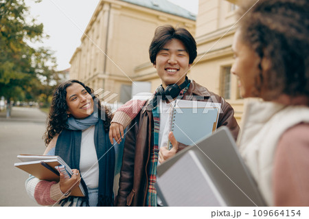 Happy students talking each other standing near university campus and holding books and laptop 109664154