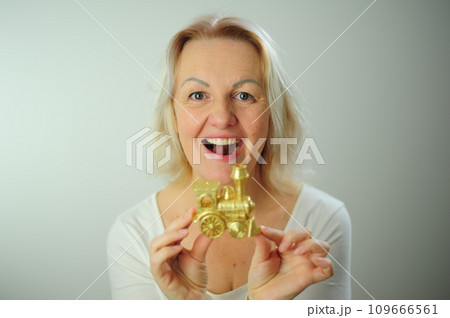 Golden steam Train toy for the Christmas tree On a white background A woman looks at a small toy steam locomotive and smiles Place for text advertising New Year and Christmas party 109666561