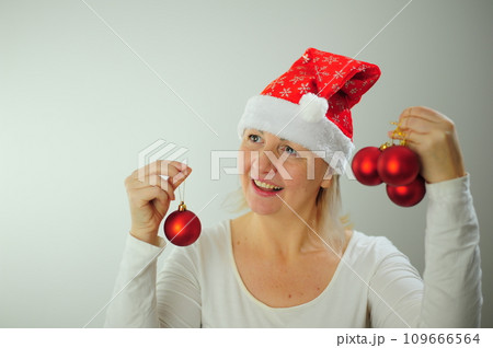 An adult woman on a white background stands smiling at her cap hat Christmas Christmas tree toys bright red New year party invitation Nice beautiful woman happy new year greetings 109666564