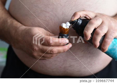 A man applies shaving foam to a shaving brush. 109667744