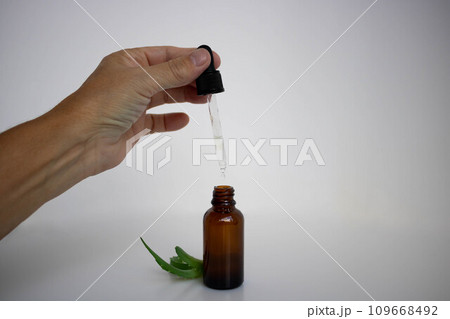 A brown bottle and a hand holding a pipette is used in cosmetology next to aloe leaves A brown bottle and a hand holding a pipette is used in cosmetology next to aloe leaves 109668492