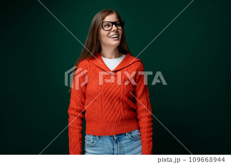 Dreamy 30 year old woman with brown hair in a red sweater on a green dark background Dreamy 30 year old woman with brown hair in a red sweater on a green dark background 109668944