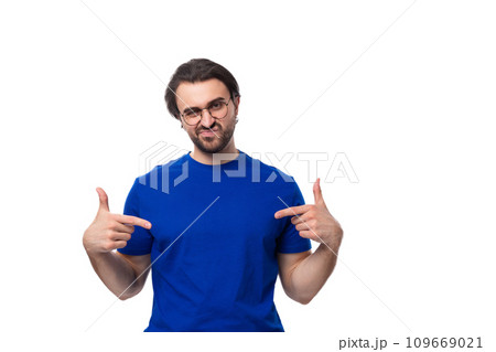 young smart brunette man with a beard dressed in a blue t-shirt points with his hand to the space 109669021