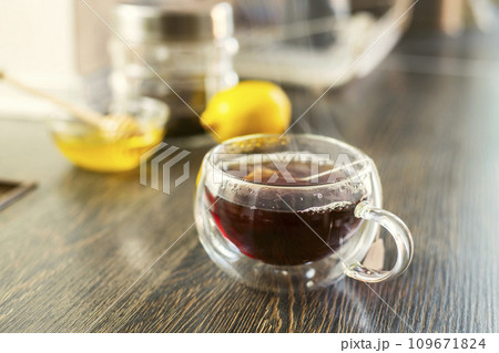 Cup of hot black tea, bowl with honey and lemon on a wooden table 109671824