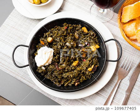 Black paella with cuttlefish ink and seafood in black pan in Spanish restaurant. Traditional dish of Spanish cuisine. Delicious dinner at restaurant 109677405