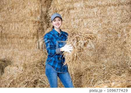 Portrait of positive female farmer with bunch of hay in her hands in the backyard of farm 109677429