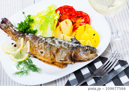 Deliciously baked whole trout with potatoes, tomatoes and greens Deliciously baked whole trout with potatoes, tomatoes and greens 109677566