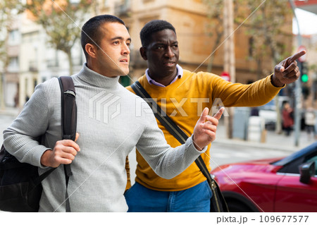 Two men walk down the street and talk on a busy street in European city. 109677577