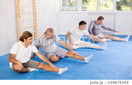 Teacher and followers perform warm-up exercises and legs stretching 109678368