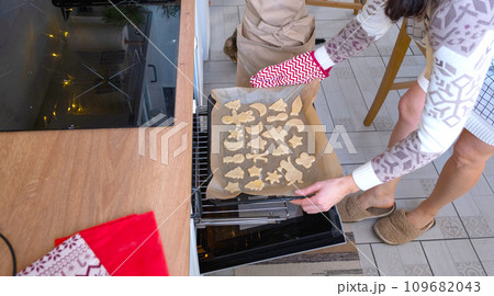 Mom puts cut-out cookies in the oven from the dough with molds on a Christmas theme in the form of a snowman, a Christmas tree, stars Mom puts cut-out cookies in the oven from the dough with molds on a Christmas theme in the form of a snowman, a Christmas tree, stars 109682043