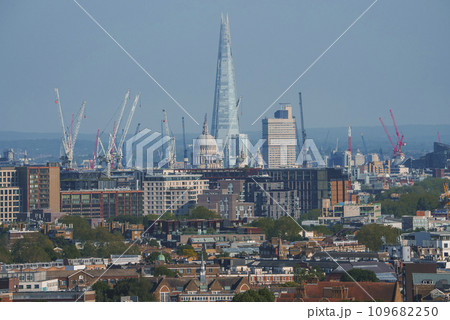 Scenic view of cityscape with blue sky in background. Skyscraper and cathedral amidst residential buildings in London. High angle view of modern development. Scenic view of cityscape with blue sky in background. Skyscraper and cathedral amidst residential buildings in London. High angle view of modern development. 109682250