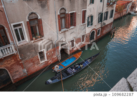 A serene scene of a blue gondola floating down a canal in Venice, Italy. The empty gondola adds to the tranquility, with picturesque buildings lining the waterway. 109682287